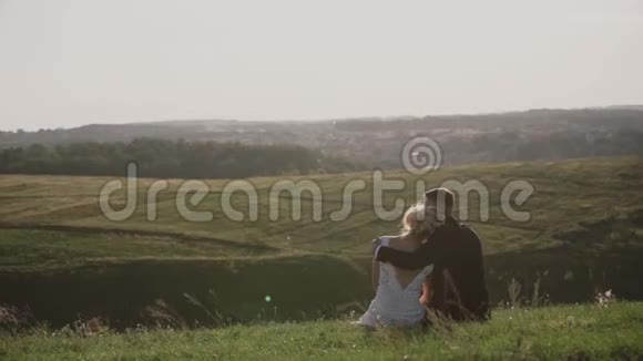 日落时在田野里情人日落时年轻人拥抱他的女朋友坐在山上视频的预览图