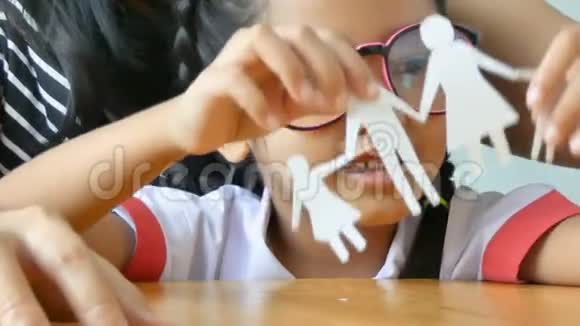 穿着泰国幼儿园学生制服的近镜头亚洲小女孩和她的母亲在玩一张白纸做成家庭形状视频的预览图