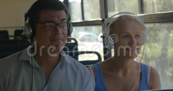 年轻夫妇在公共汽车上听着耳机里的音乐他们跟着音乐跳舞男人唱歌视频的预览图