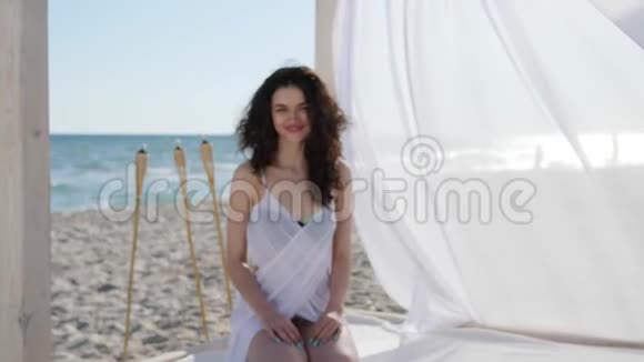 暑假期间坐在海边的女人卷发的快乐女人海滩上的肖像美女美女视频的预览图