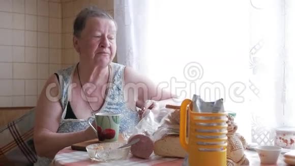 一位老妇人端着一杯热饮和饮料他坐在窗边吃早餐简单的家居服视频的预览图