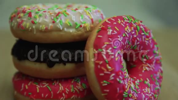 巧克力中的甜甜圈粉釉中的甜甜圈奶油釉中的甜甜圈躺在桌子上视频的预览图