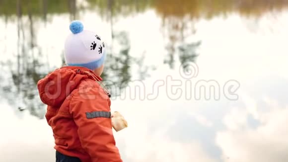 一个孩子站在池塘边扔石头在新鲜空气中游走视频的预览图