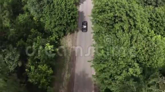 绿色森林背景下乡村公路上行驶的无人机视野黑车视频的预览图