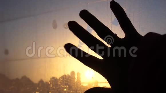 靠近女性的手在夕阳背景下触摸汽车里的湿窗视频的预览图