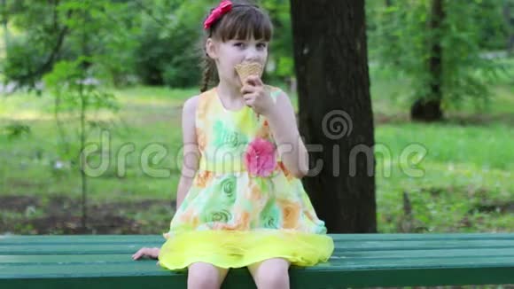 漂亮的小女孩坐在长凳上夏天吃冰淇淋视频的预览图
