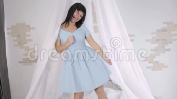 穿着蓝色裙子的漂亮年轻女子在床上玩得很开心视频的预览图