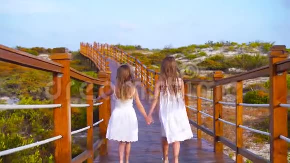 小可爱的女孩在去白色热带海滩的路上的木桥上视频的预览图