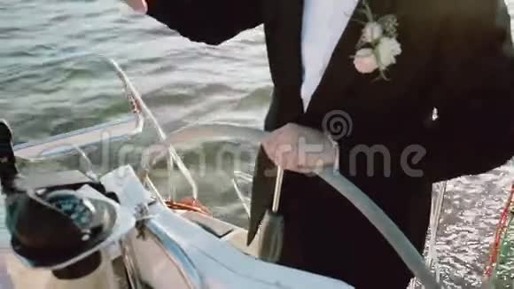 在游艇上新郎穿着婚纱站在方向盘后面的特写镜头在海上驾驶这艘船的人视频的预览图