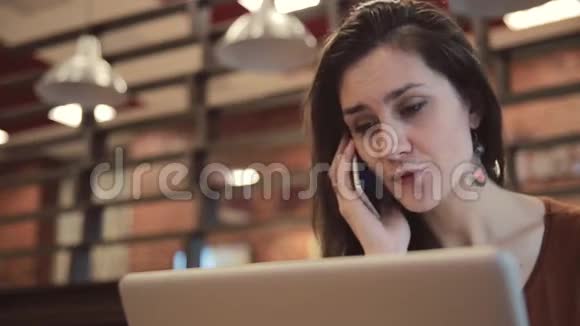 年轻的黑发女孩在笔记本电脑上工作在咖啡馆里打电话视频的预览图