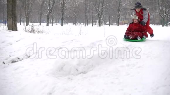 两个快乐的男孩坐在雪城公园的滑梯旁视频的预览图