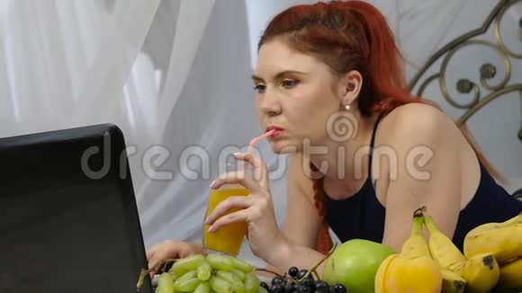 在床上享受的年轻女人用笔记本电脑和喝橙汁慢动作视频的预览图