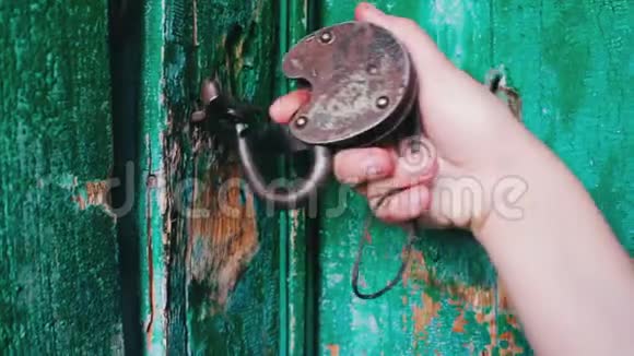 旧的老式铁锁在门上绿色油漆剥落女性手打开和关闭锁视频的预览图