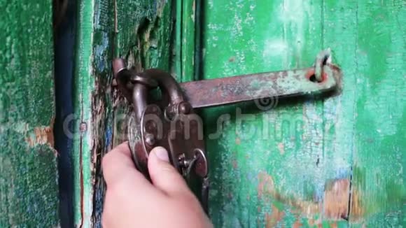 旧的老式铁锁在门上绿色油漆剥落女性手打开和关闭锁视频的预览图