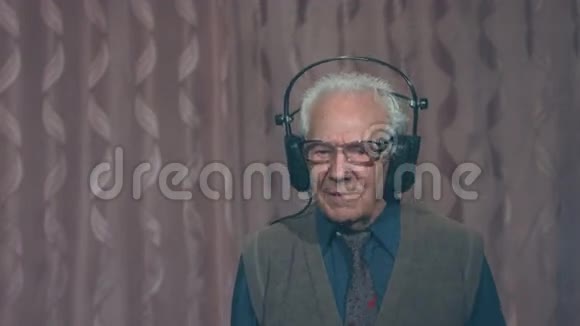 带耳机的粉红色背景上的白发爷爷的肖像2次射击视频的预览图