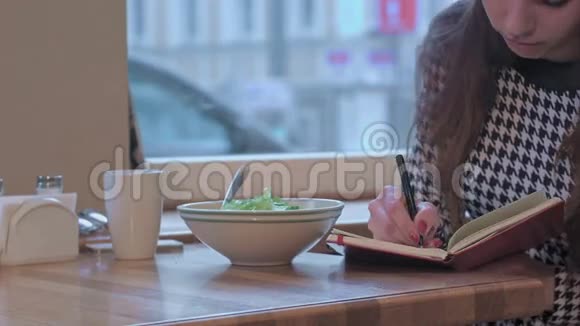 年轻女商人在记事本上写作的武器她正坐在咖啡馆的桌子旁吃着沙拉视频的预览图
