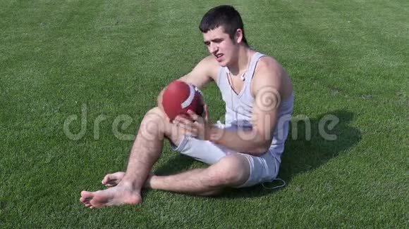 年轻运动员带着橄榄球坐在草地上视频的预览图