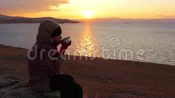 女孩坐在海边喝热茶令人惊叹的金色日落视频的预览图
