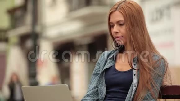 这个女孩在街上的电脑上工作在电话里交谈特写镜头视频的预览图