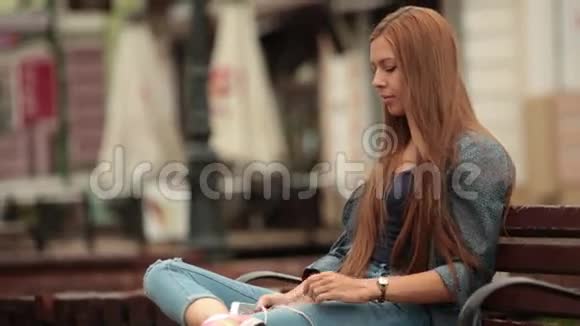 带着耳机和电话坐在长凳上听音乐的年轻女孩视频的预览图