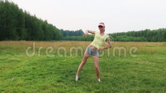 穿短裤戴帽子的漂亮女孩在绿色草地上跳舞视频的预览图