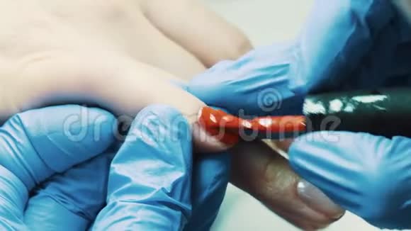 美容用手在美容院的拇指指甲上涂红色指甲油视频的预览图