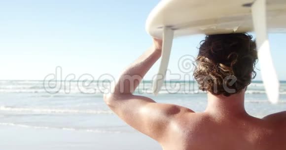 阳光明媚的一天一个人在沙滩上背着冲浪板视频的预览图