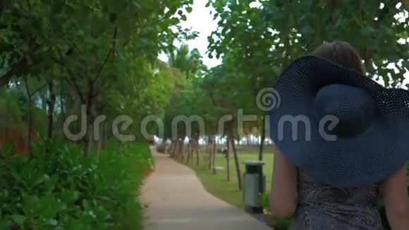 戴着蓝帽子的年轻女孩正穿过一个热带公园夏日时光慢动作视频的预览图