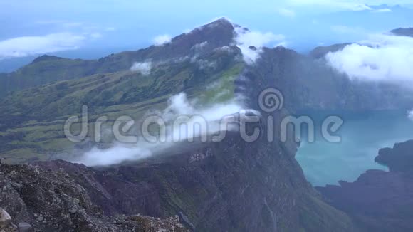 在印度尼西亚的Rinjani巨大的徒步旅行石山链白云之间平静的湖面上令人惊叹的空中4k景色视频的预览图