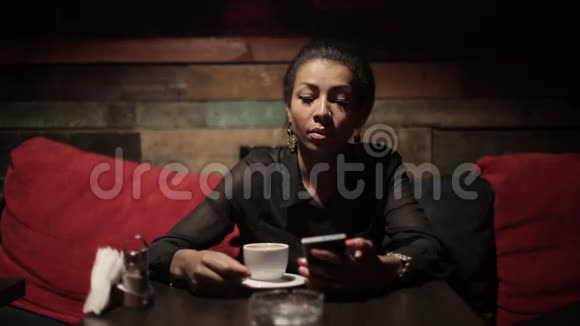黑人妇女喝热咖啡使用智能手机视频的预览图