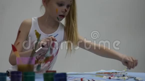 小女生可爱的小女孩画家在桌子上画画在她的衣服上画画慢动作视频的预览图