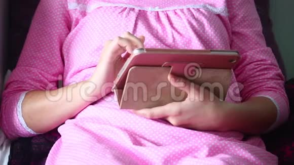 一个穿睡衣的女人躺在床上用平板电脑工作她用手指触摸屏幕视频的预览图