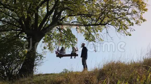 爸爸在树下的秋千上摇动她的女儿视频的预览图