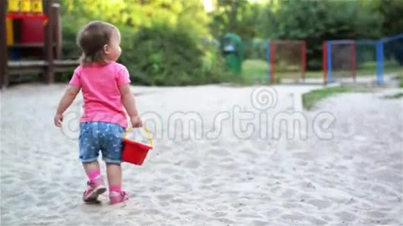 小可爱的女孩宝宝在操场上玩沙箱沙堆在桶里然后拿着桶走视频的预览图