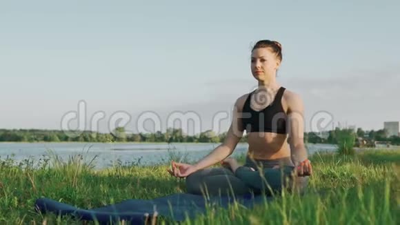 日出时在莲花位置的漂亮女孩早上在湖边做瑜伽的女人视频的预览图