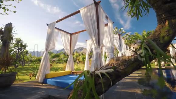 游泳池山脉和弗兰吉帕尼附近有白色窗帘的豪华日光浴床视频的预览图