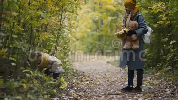 小女儿和妈妈一起在秋天公园散步玩耍躲在树叶后面视频的预览图