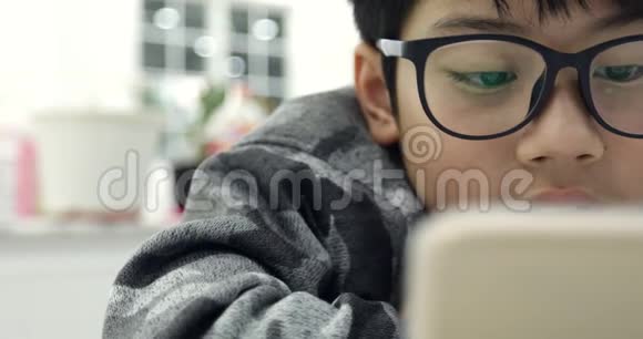 可爱的亚洲男孩戴着眼镜使用平板电脑年轻的十几岁男孩在数字平板电脑上玩游戏视频的预览图