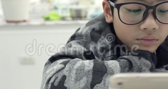 可爱的亚洲男孩戴着眼镜使用平板电脑年轻的十几岁男孩在数字平板电脑上玩游戏视频的预览图