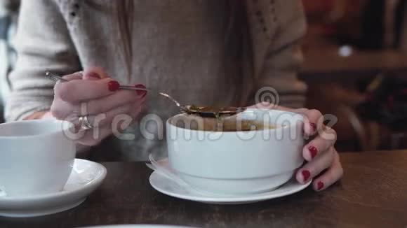 在咖啡馆里用勺子从白色的碗里吃汤的红指甲女人的手的特写镜头4K视频的预览图