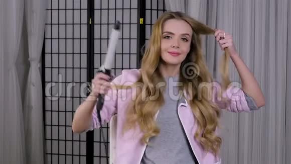 年轻的金发女郎用钳子卷头发做发型视频的预览图