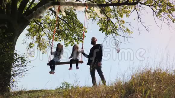 爸爸在树下的秋千上摇动她的女儿视频的预览图