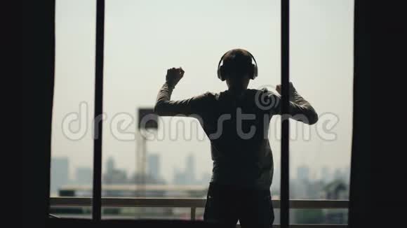 站在酒店阳台上的有线耳机里的年轻人跳舞和听音乐剪影视频的预览图