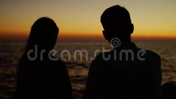 两人坐在海边看日落看着镜头视频的预览图