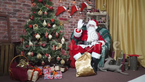 圣诞老人坐在圣诞树旁的椅子上挥舞着手视频的预览图