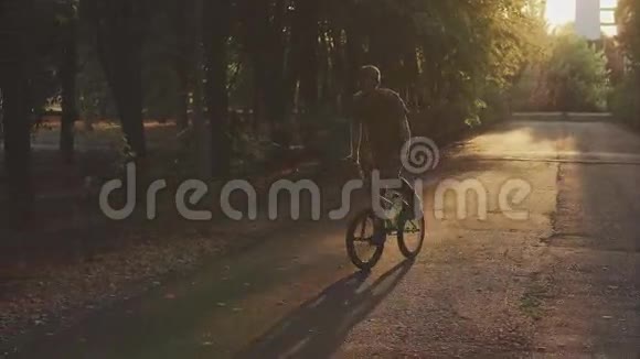 一个穿着自由风格的人骑着自行车骑着高大的树在公园里视频的预览图