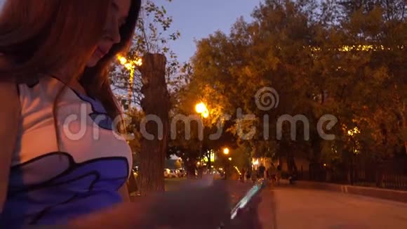 穿着红色指甲油的布鲁内特女孩在晚上的街道上使用她的智能手机4K视频视频的预览图