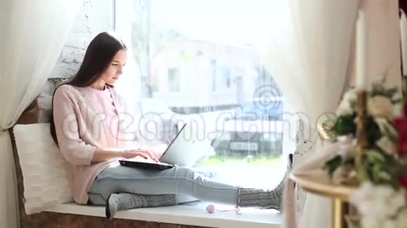 年轻漂亮的女人坐在窗口在电脑上工作视频的预览图
