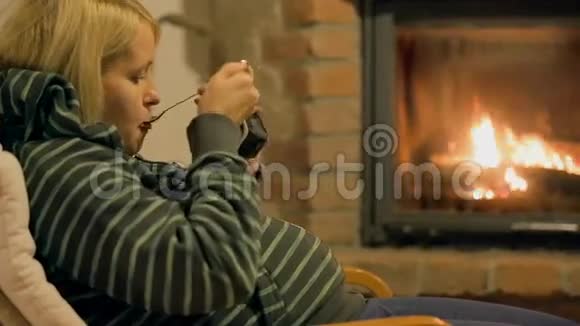 金发女性在燃烧木头的壁炉前吃布丁视频的预览图