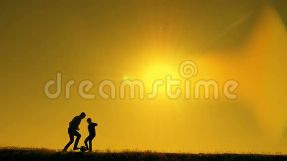 日落时分父亲和儿子在公园里踢足球在灿烂的阳光下剪影视频的预览图